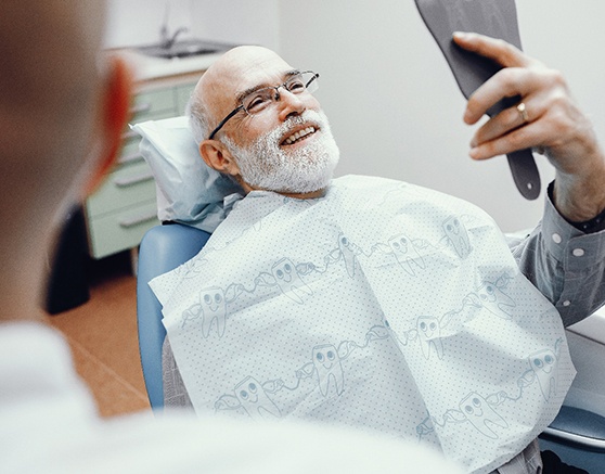 An older man admiring his smile with a hand mirror