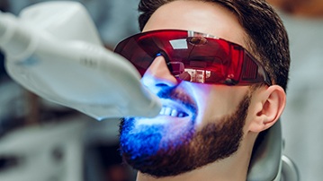 Man with brown hair undergoing teeth whitening procedure in dental office