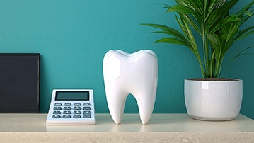 A calculator, model tooth, and potted plant on counter with teal background