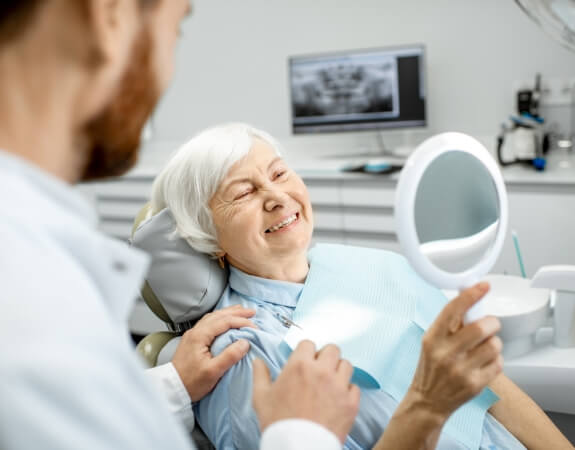 Woman looking at smile after tooth replacement with dental implants