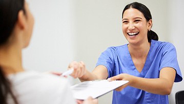 Smiling dental assistant handing patient forms