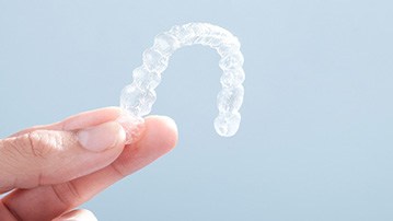 Patient holding Invisalign clear aligner against blue background