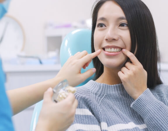 Woman pointing to smile after tooth replacement with dental implants