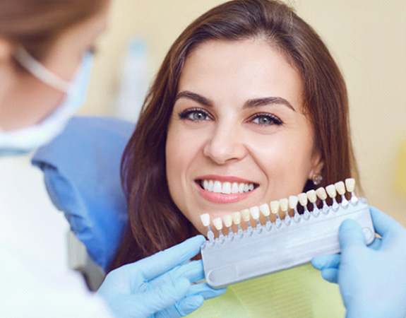 A dentist using a shade guide on a woman’s smile