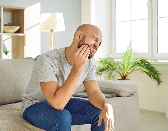 Man experiencing toothache while sitting on couch at home