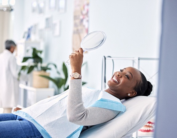 Woman smiling at reflection in handheld mirror at dentist's office